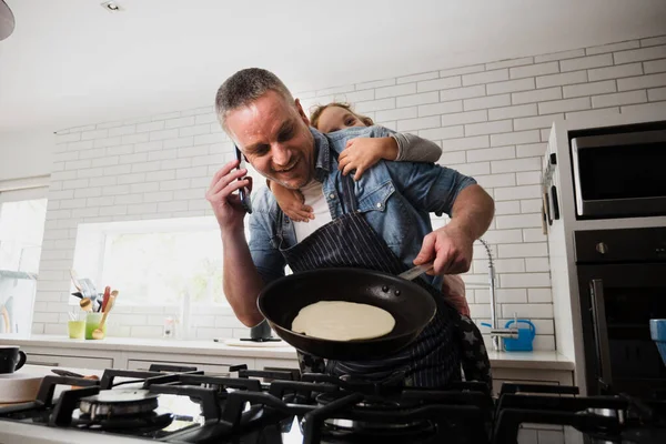 Pai e filha se unindo enquanto assando panquecas conversando no smartphone na cozinha. — Fotografia de Stock
