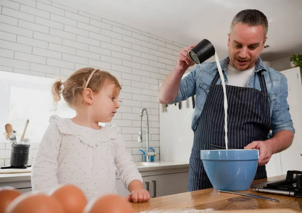 Pai derramando ingredientes em cozimento intestinal com filha na cozinha organizada. — Fotografia de Stock