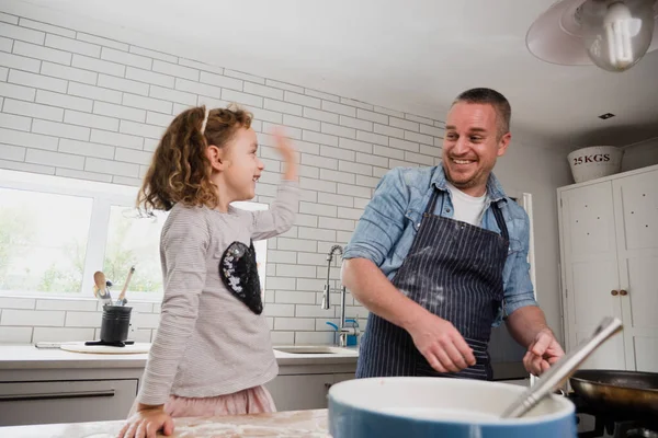 Pai feliz e filha criança assar juntos na cozinha, filha jogando farinha no pai — Fotografia de Stock