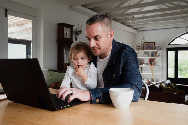 Caucasian father getting work done on laptop while daughter sitting on his lap