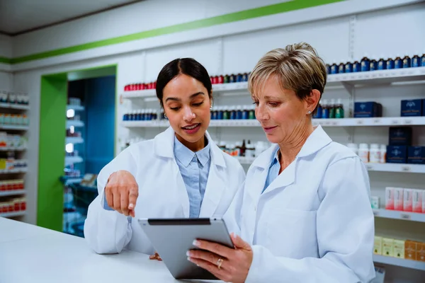 Caucasian pharmacist manager helping new mixed race intern use digital tablet standing in. pharmacy drugstore