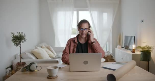 Caucásico macho trabajando desde casa mecanografía en el ordenador portátil, mientras que el chat en el dispositivo celular — Vídeos de Stock