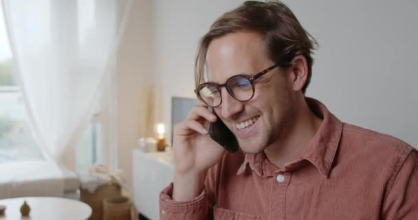 Caucasiano estudante do sexo masculino conversando no dispositivo celular que trabalha em casa — Vídeo de Stock