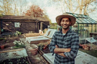 Açık havada duran melez ırk çiftçisi yeşil örneklerle seraya bakıyor.