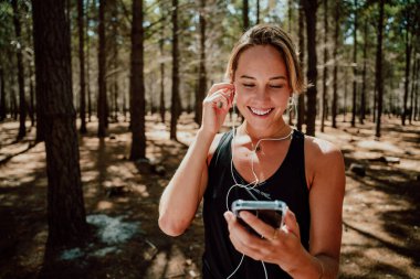 Beyaz kadın sporcu ormanda egzersiz yapıyor kulaklıkla müzik dinliyor. 