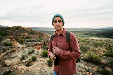 Beyaz erkek kampçı dağda yürüyor elinde su şişesiyle vahşi doğayı kucaklıyor. 