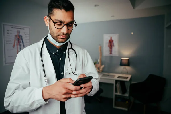 Mixte race mâle infirmière textos sur dispositif cellulaire debout dans la clinique — Photo