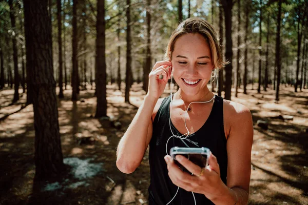 Beyaz kadın sporcu ormanda egzersiz yapıyor kulaklıkla müzik dinliyor. 