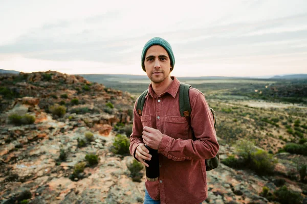 Beyaz erkek kampçı dağda yürüyor elinde su şişesiyle vahşi doğayı kucaklıyor. 