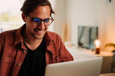 Projeyi bitirirken dizüstü bilgisayarla gülümseyen beyaz erkek öğrenci 