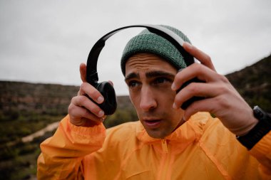 Genç erkek sporcu, soğuk havada çakıllı dağ yolunda koşmadan önce uygulamadan müzik için kulaklık kullanıyor.