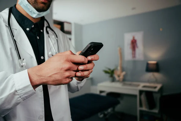 Mixte race infirmière masculine debout dans le bureau textos sur l'appareil cellulaire — Photo