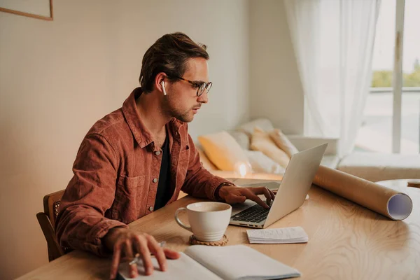 家庭で働く白人男性がノートパソコンでホットコーヒーを飲みながら — ストック写真