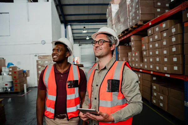 Kafkas erkek işçi dijital tablet tutuyor. Fabrika atölyesinde melez bir meslektaşla gülümsüyor.