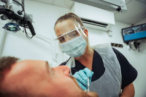 Καυκάσιος άντρας πελάτης κάθεται στην καρέκλα του οδοντιάτρου ενώ η νοσοκόμα χειρουργεί σπασμένο δόντι — Φωτογραφία Αρχείου