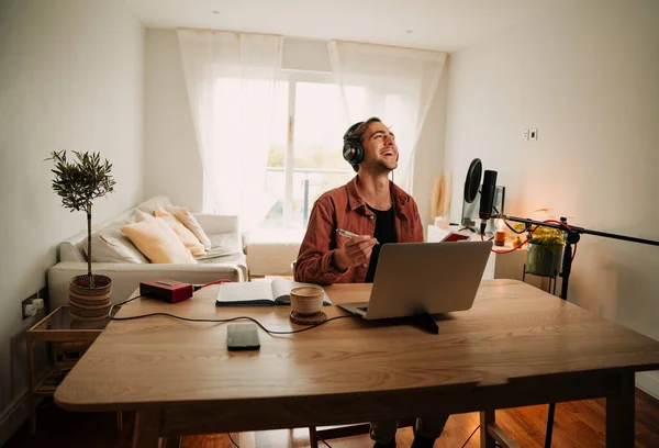 Kaukasische männliche Podcaster hören Anrufe von Zuhörern, die lachen, während sie Notizen aufschreiben — Stockfoto