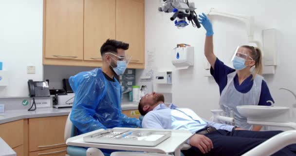 Kaukasiska kvinnliga och manliga läkare flyttar röntgen maskin för att undersöka manliga patienter tandproblem — Stockvideo