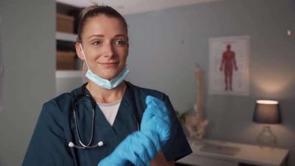 Enfermeira branca em pé no consultório médico colocando luvas cirúrgicas — Vídeo de Stock