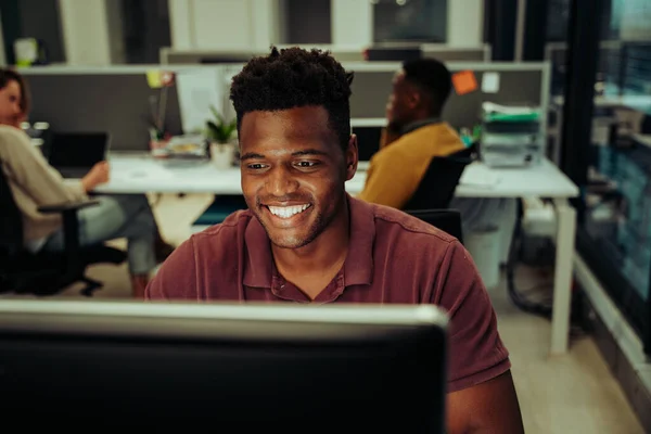 Imprenditore maschio sorridente che invia email a colleghi e manager che lavorano fino a tardi in ufficio — Foto Stock