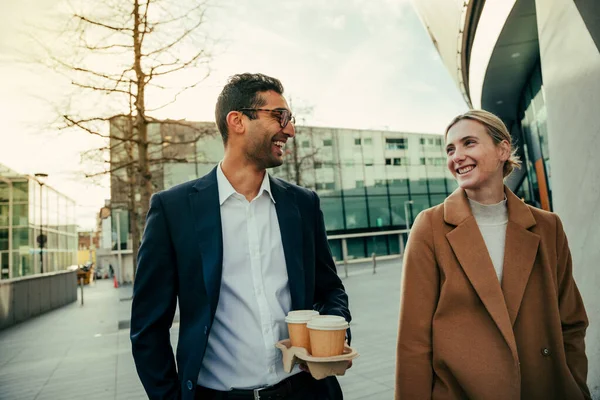 Sorridenti colleghi di razza mista che si legano mentre camminano al lavoro godendo di caffè caldo e idee di brainstorming — Foto Stock
