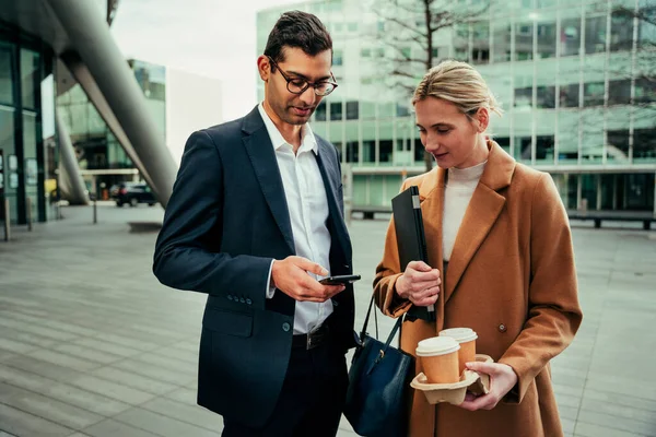 Caucásico mujer y mixta raza hombre de negocios charlando mientras mecanografía en el teléfono celular beber café caliente — Foto de Stock