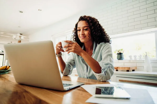 在家里工作的混血女学生一边喝着热咖啡一边看笔记本电脑 — 图库照片