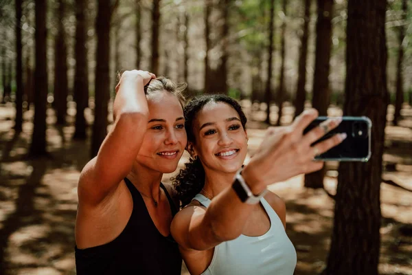 Δύο φίλοι χαμογελώντας για selfie σε κυτταρική συσκευή στέκεται στο δάσος — Φωτογραφία Αρχείου