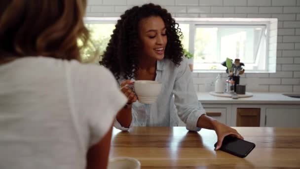 Blandade ras kvinnliga vänner koppla av tillsammans dricka kaffe rulla på sociala medier på cellulär enhet — Stockvideo
