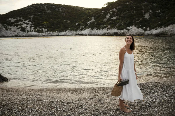 Beyaz kadın sahilde sandaletle yürüyor.