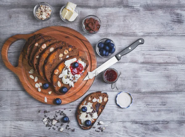 On a light wooden table sliced bread with fruits and nuts — Zdjęcie stockowe