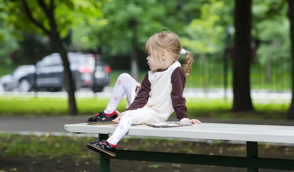 Mała dziewczynka siedzi na ławce z książką — Zdjęcie stockowe