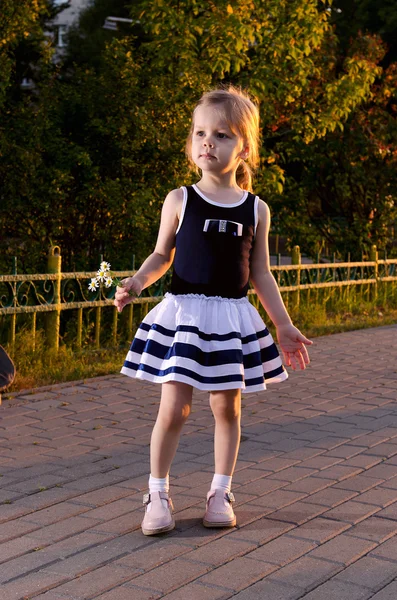 Petite fille regardant le coucher du soleil et tenant des marguerites — Photo