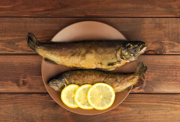 En la mesa de madera hay un plato con dos pescados horneados — Foto de Stock