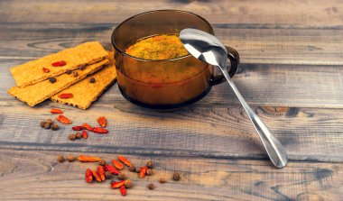 On the wooden table is a glass cup of soup with parsley