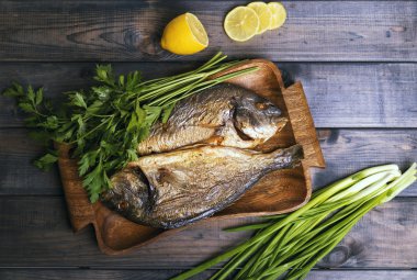On a wooden table plate with two roasted carp fish dorado