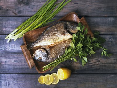 On a wooden table plate with two roasted carp fish dorado