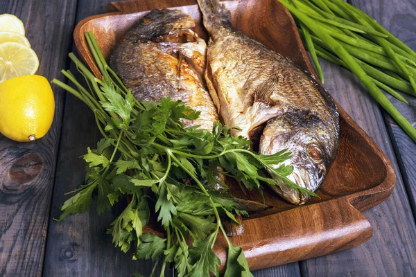 On a wooden table plate with two roasted carp fish dorado — 图库照片