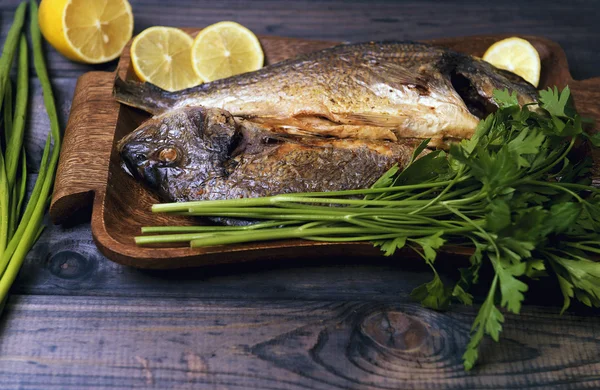 On a wooden table plate with two roasted carp fish dorado — Stock Fotó