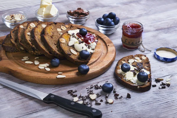 On a light wooden table sliced bread with fruits and nuts — 스톡 사진