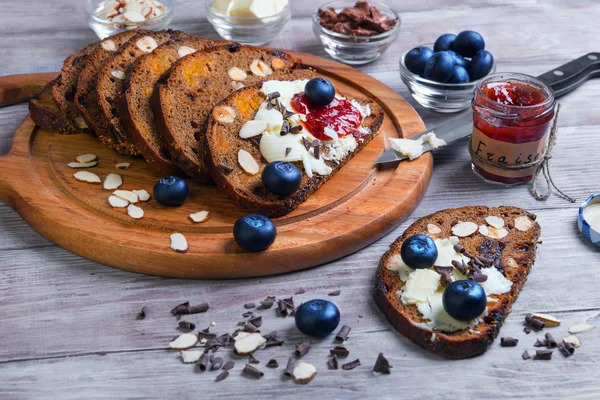 On a light wooden table sliced bread with fruits and nuts