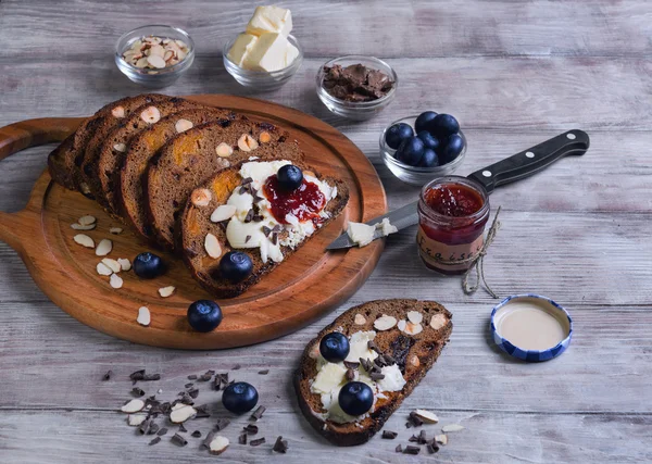 Em uma mesa de madeira leve pão fatiado com frutas e nozes — Fotografia de Stock