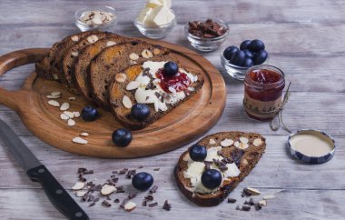 On a light wooden table sliced bread with fruits and nuts