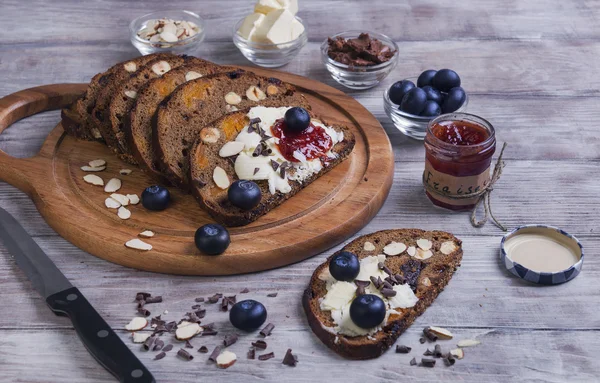 Em uma mesa de madeira leve pão fatiado com frutas e nozes — Fotografia de Stock