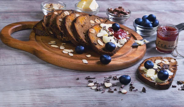 On a light wooden table sliced bread with fruits and nuts