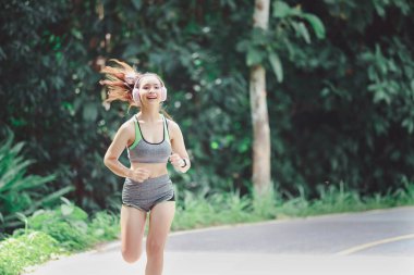 Genç bayan koşucu sabah yolda koşarken kulaklıkla müzik dinliyor..