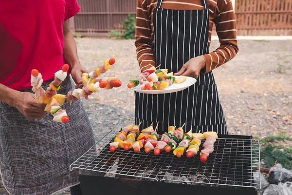 A woman with a barbecue plate and a man grilling barbecue and pork in dinner party. Food, people and family time concept.