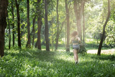 Genç bayan koşucu kulaklıkla müzik dinlerken sabahları tropikal yağmur ormanlarında koşuyor..
