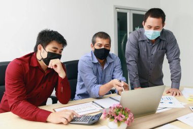 Koruyucu maskeler takan iş adamları toplantı odasında tartışıyor ve birlikte çalışıyorlar. Sosyal mesafe uygulaması Coronavirus COVID-19 'u engelliyor.