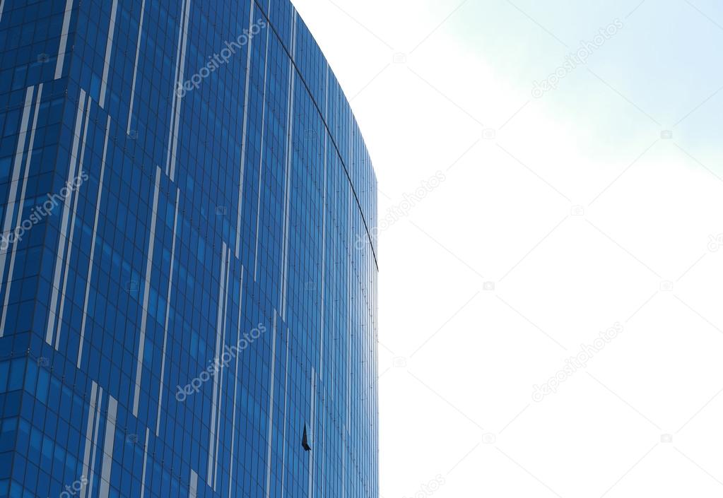 Glass facade of an urban office building reflecting clouds on a sunny day