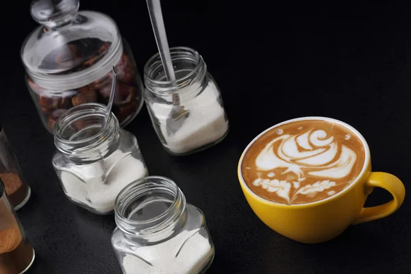 Cup of cappuccino and sugar bowls on dark background. Latte art — Stock Photo, Image